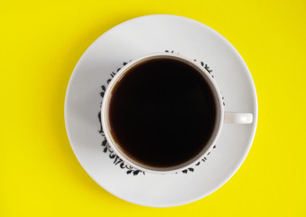white mug with coffee on an isolated yellow background top view