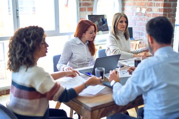 Group of business workers smiling happy working together. Sitting with smile on face using laptop reading documents at the office