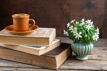 Bouquet of forest flowers hepatice in vase, old books, coffee cup on wooden table. Cozy home, reading, breakfast, hygge, evening, library, rest, education concept. Copy space