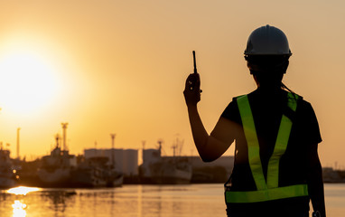 Silhouette of an engineer, technician woman standing by the shipping port in her hand holding radio...