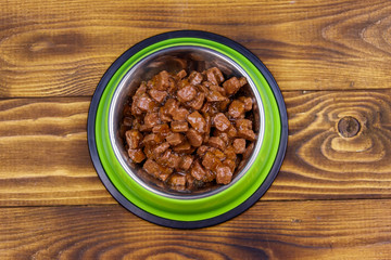 Canned food for cats or dogs in green metal bowl on wooden floor. Top view