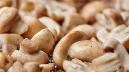 Sliced toasted champignon close-up. Mushrooms are fried in oil in a pan background