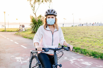 Portrait of a woman with protective safety mask on her face riding a bike on a bike path in the city on a sunny day.