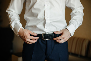 A stylish man puts on a leather belt close-up. Fashion