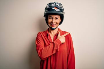 Middle age motorcyclist woman wearing motorcycle helmet over isolated white background cheerful with a smile of face pointing with hand and finger up to the side with happy and natural expression