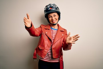 Middle age motorcyclist woman wearing motorcycle helmet and jacket over white background looking at the camera smiling with open arms for hug. Cheerful expression embracing happiness.