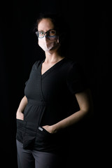 Clinician or nurse in black scrubs with n95 covid mask in dramatic dark lighting