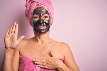 Middle age brunette woman wearing beauty black face mask over isolated pink background Swearing with hand on chest and open palm, making a loyalty promise oath