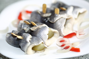 Pickled herrings called rollmops with pieces of onion and red pepper on plate macro close up