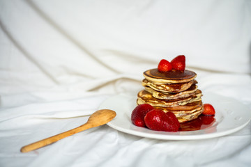 Close-up delicious pancakes, with strawberries and syrup on a light background. Sweet syrup flows from a stack of pancake