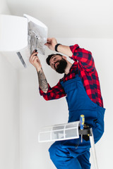 Young bearded handyman repairing air conditioner.