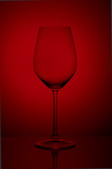 The crystal glass stands on the reflecting surface on a red background. studio photo. product. Beautiful shadow from wine glass. macro photo