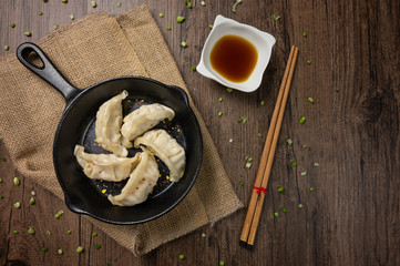 Gyozas, fried japanese dumplings on cast-iron pan served with soy sauce. wooden texture background. Top view. Flat lay with copy space