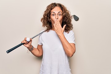 Middle age beautiful sportswoman playing golf using stick and ball over white background covering mouth with hand, shocked and afraid for mistake. Surprised expression