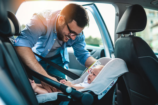 Young father putting his baby boy on a safety child car seat.