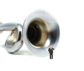 A businessman makes a speech while presenting in front of a large silver horn - Tiny People Working From Home