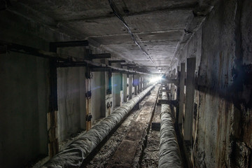 Underground concrete utility tunnel with pipes and wires. Utility tunnel with light in the end.