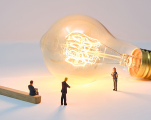 A businesswoman is lit by a large filament lightbulb (idea) as she presents to colleagues - Tiny...