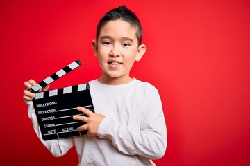 Young little boy kid filming video holding cinema director clapboard over isolated red background...