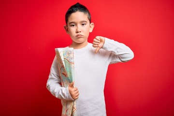 Young little boy kid looking at turist city destination map over red isolated background with angry...
