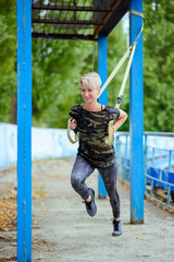 young girl doing exercises outdoors using slings, TRX loop