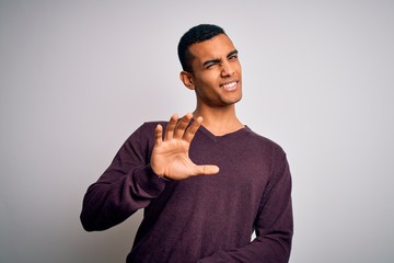 Young handsome african american man wearing casual sweater over white background disgusted expression, displeased and fearful doing disgust face because aversion reaction. With hands raised