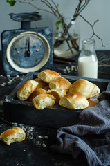Fresh homemade buns in a wooden box against the background of old scales and a bottle of milk.