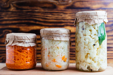 Fermented vegetables cabbage, cauliflower, carrot in glass jar on wood background.