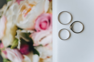 Wedding gold rings lie on a white table against the background of colorful flowers. Photography, concept, top view.