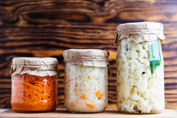 Fermented vegetables cabbage, cauliflower, carrot in glass jar on wood background.