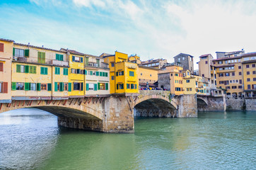 Famous Ponte Vecchio Bridge, medieval stone bridge over the Arno River in Florence, Tuscany, Italy. Major landmark of the Italian city. Colorful houses on the construction. Horizontal photo.
