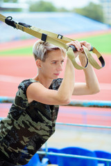 young girl doing exercises outdoors using slings, TRX loop