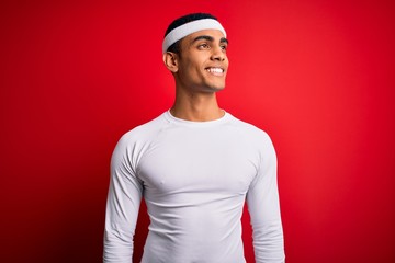 Young handsome african american sportsman wearing sportswear over red background looking away to side with smile on face, natural expression. Laughing confident.