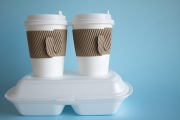 Fototapeta na wymiar Coffee in disposable glasses with a lid and a container with takeaway food on a blue background and space for copying. Concept delivery.