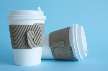 Two white disposable coffee cups close up on a blue background and a copy space