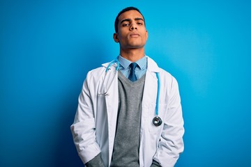 Handsome african american doctor man wearing coat and stethoscope over blue background looking...
