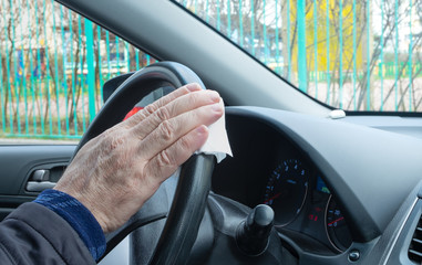 A close-up of a man's hand wipes the steering wheel of a car with a napkin with an antiseptic. Protection from coronavirus, hygiene concept. Horizontal orientation, selective focus.