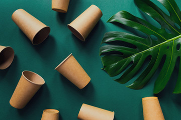 Eco friendly craft paper cups on green background with monstera leaf