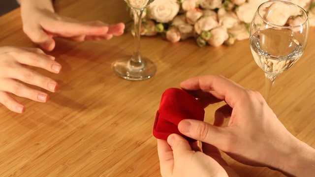 Closeup shot of marriage proposal. Man gives ring with diamond to woman proposing marriage. Indoors restaurant or home, romantic dinner