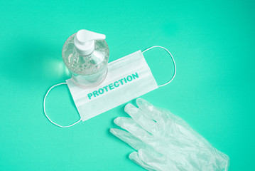 Container with alcohol gel, gloves and surgical mask on the light blue background