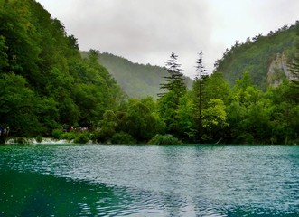 Imagen primaveral de pasarelas flotantes de madera junto a cascadas y lagos azules con antiguos...