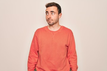 Young handsome man with blue eyes wearing casual sweater standing over white background smiling looking to the side and staring away thinking.