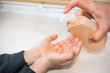 Closeup father hand applying bottle pump dispenser sanitizer alcohol gel cleaning hands little child COVID-19 or coronavirus protection concept, with copy space.