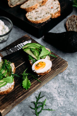 Whole grain bread sandwich with avocado, arugula, egg and cream cheese on a table