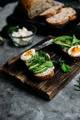 Whole grain bread sandwich with avocado, arugula, egg and cream cheese on a table