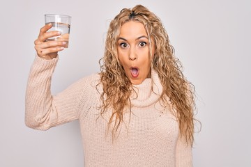 Young beautiful blonde woman drinking glass of water over isolated white background scared and amazed with open mouth for surprise, disbelief face
