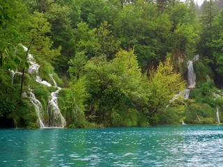 Imagen primaveral de pasarelas flotantes de madera junto a cascadas y lagos azules con antiguos...