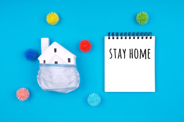 Cute little house covered with medicine mask and plastic balls as viruses on blue with Stay home wording. Epidemic, social isolation, coronavirus COVID-19 concept. Option with text