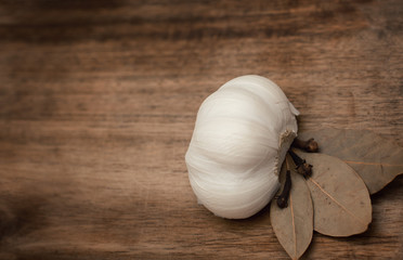 garlic, salt, bay leaf, clove spices lie on a wooden surface