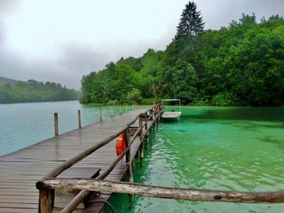 Fototapeta na wymiar Imagen primaveral de pasarelas flotantes de madera junto a cascadas y lagos azules con antiguos embarcaderos y barcas de remos en plena naturaleza en el Parque Nacional de los Lagos de Plitvice